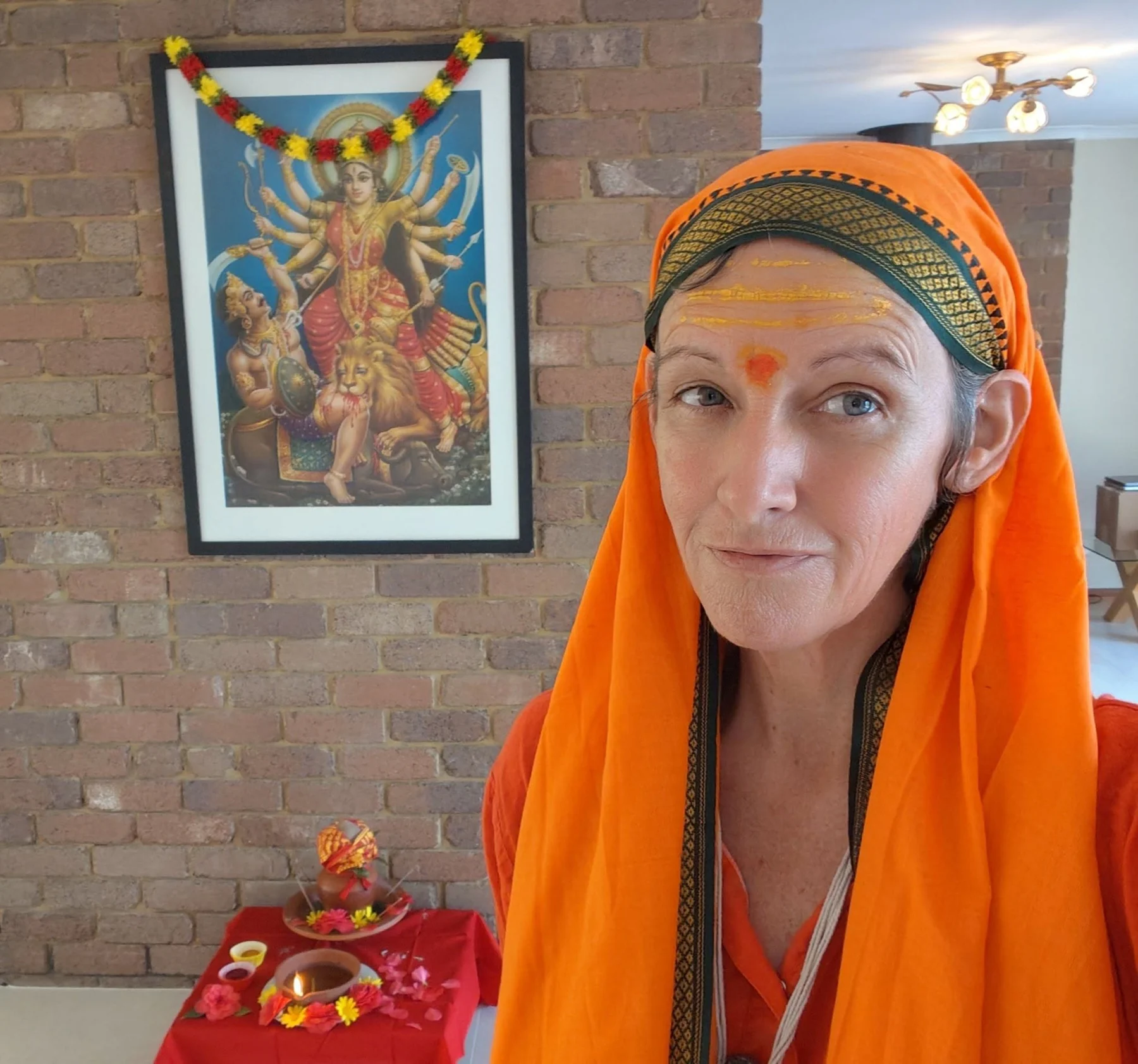 A woman in an orange head covering beside a small shrine